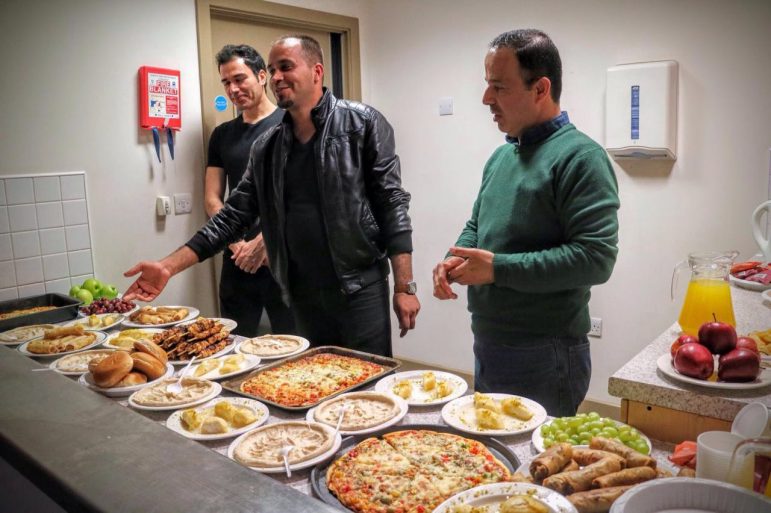 Adnan (centre) with two other Syrian volunteers with a selection of food they had prepared for members of an English class they attend. s